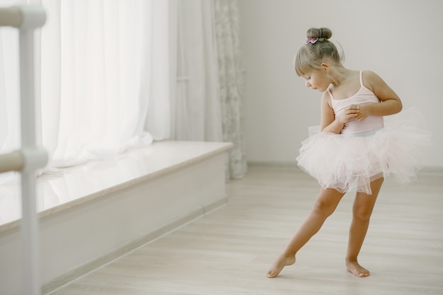 ピンクのバレエ衣装のかわいい小さなバレリーナ。トウシューズを履いた子供が部屋で踊っています。ダンスクラスの子供。