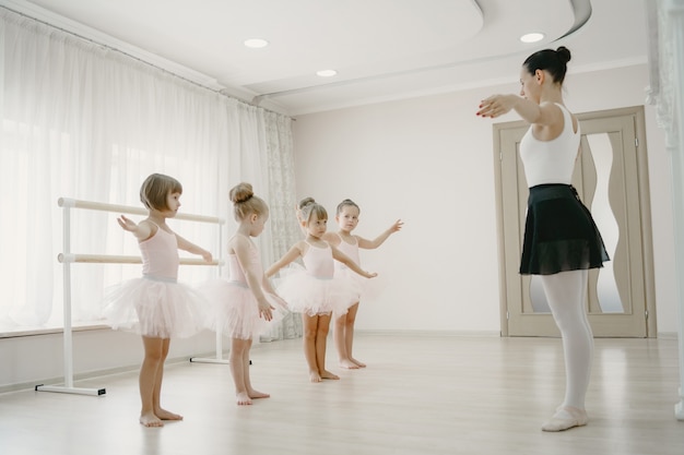 Симпатичные маленькие балерины в розовых балетных костюмах. Дети в пуантах танцуют в комнате. Ребенок в танцевальном классе с учителем.