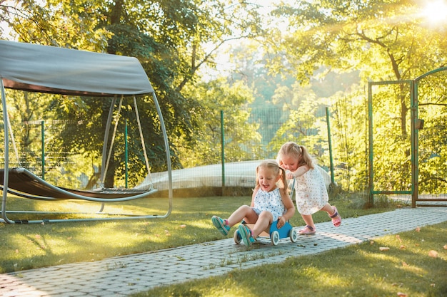 Cute little blond girls riding a toy car in summer.