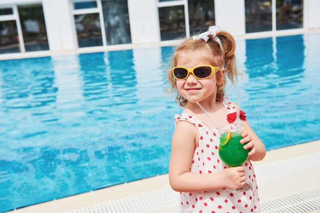 Cute little blonde at the pool and holding achild's cocktail .