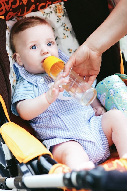 Piccolo neonato sveglio degli occhi azzurri con imbottiglia il passeggiatore