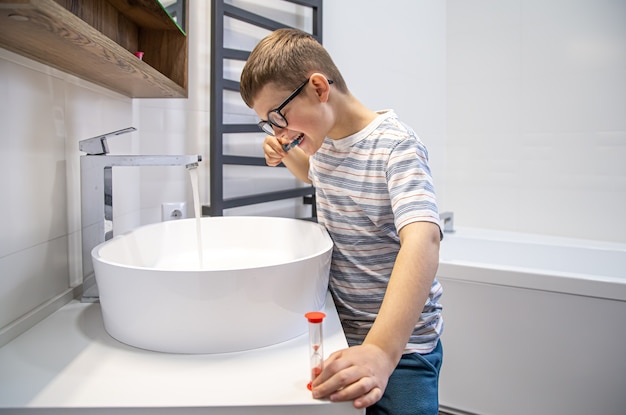 Foto gratuita un simpatico ragazzino che si lava i denti e cronometra l'ora con una clessidra.