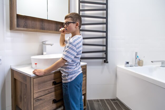 A cute little boy brushing his teeth and timing the hour with an hourglass.