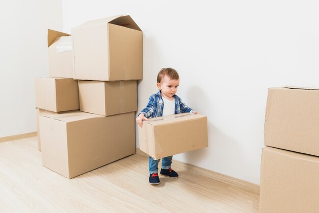 Cute little boy carrying cardboard boxes at new home