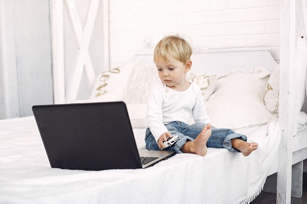 Cute little boy playing with a laptop on a bed