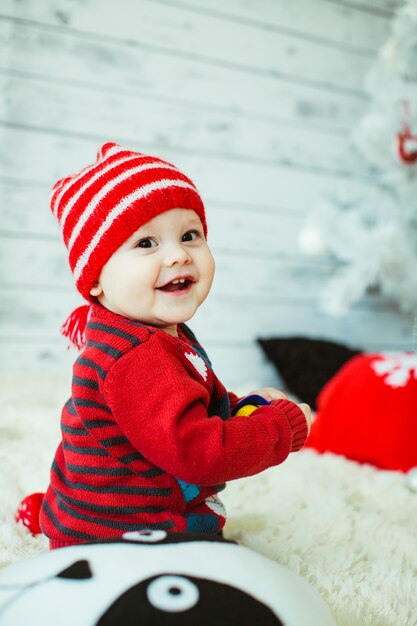 Cute little boy in a red striped hat sits on the floor