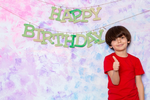 Cute little boy in red t-shirt decorating colorful wall with happy birthday words