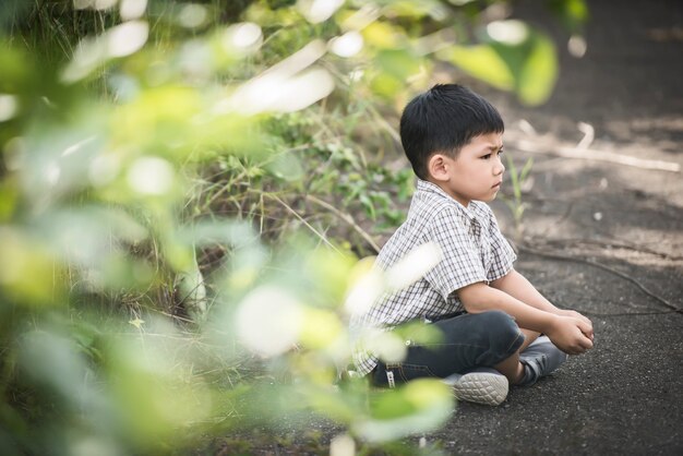 Cute little boy sitting on the ground in the summer park.