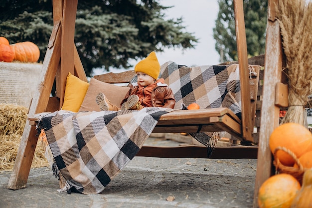 Cute little boy sitting on swing with halloween pumpkins at ranch