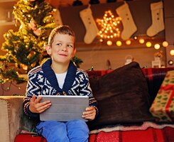 The cute little boy using a tablet pc in a room with christmas holiday decoration.