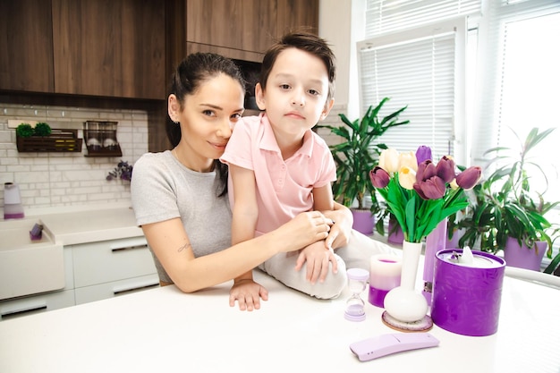 Ragazzino carino con madre felice nella cucina luminosa che guarda l'obbiettivo con sorrisi sui volti famiglia felice in una cucina a casa