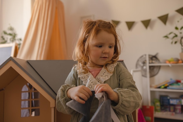 Cute little caucasian girl with red hair wears casual clothes and spends time in her room with toys Children concept