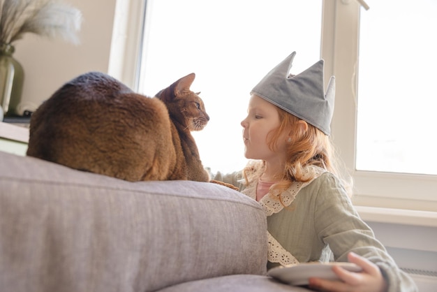 Cute little caucasian redhead girl 23 years old with pet cat at window in morning Lifestyle concept