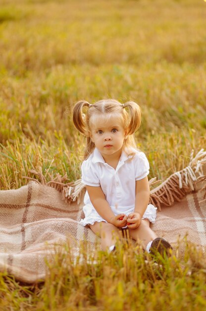 Cute little child in white dress posing on green field and