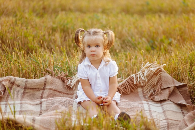 Cute little child in white dress posing on green field and