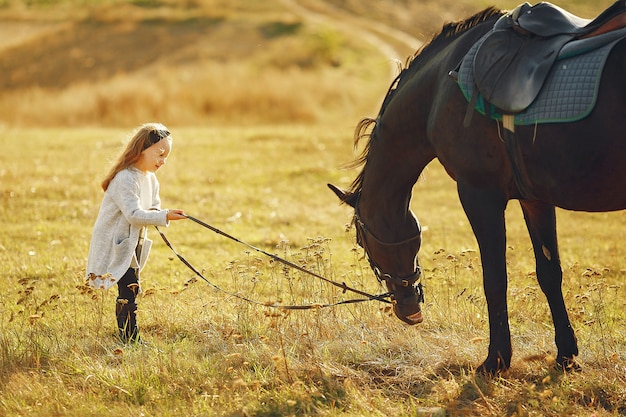 Милая маленькая девочка в осеннем поле с лошадью