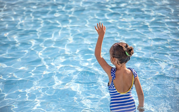 Cute little girl bathes in a pool in clear water.