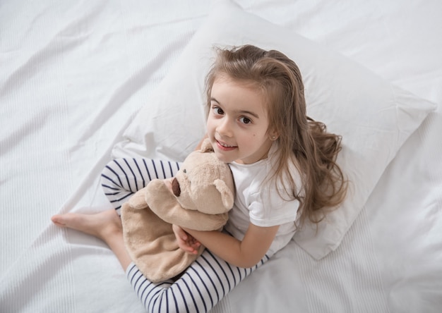 Cute little girl in bed with soft toy.