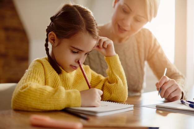 Cute little girl doing homework with help of her mother