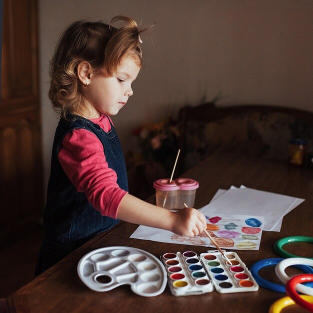 Милая маленькая девочка рисует круг из разноцветных красок
