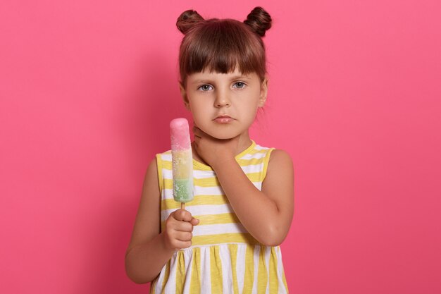 Милая маленькая девочка ест мороженое и болит горло