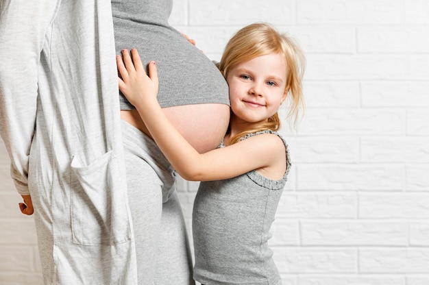 Cute little girl embracing mother pregnant belly