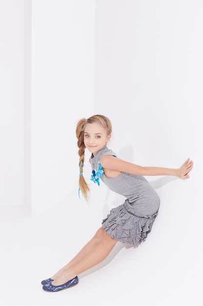 Cute little girl in grey dress sits white studio background.