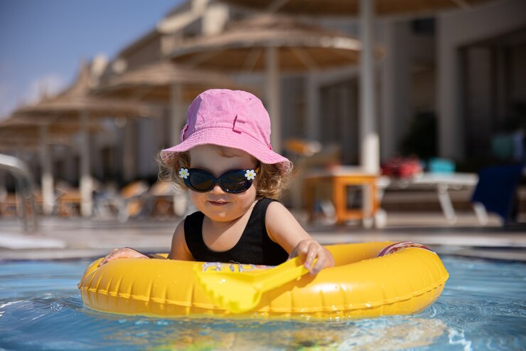 無料Photo 帽子とサングラスのかわいい女の子が水泳サークルに座っている間プールで遊ぶ