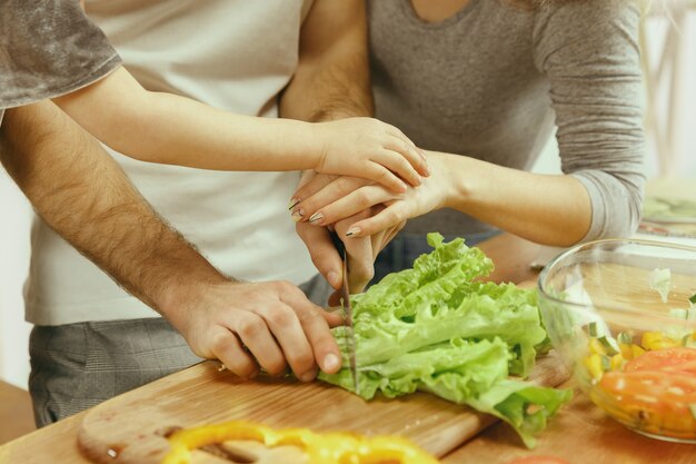 Cute little girl and her beautiful parents are cutting vegetables