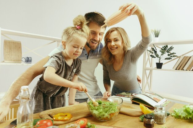 Cute little girl and her beautiful parents are cutting vegetables