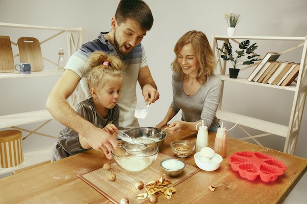 Bambina sveglia ed i suoi bei genitori che preparano la pasta per la torta in cucina a casa. concetto di stile di vita familiare
