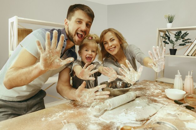Cute little girl and her beautiful parents preparing the dough for the cake in kitchen at home