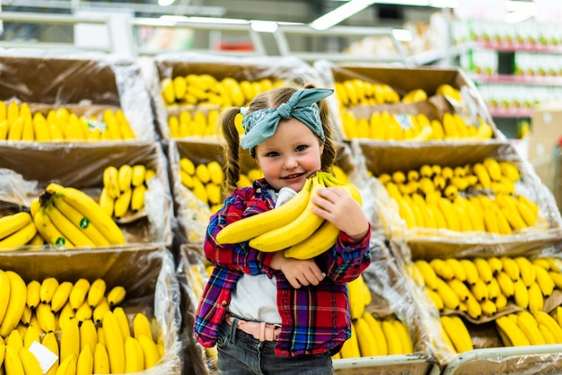 Cute little girl holding bananas in a food store or supermarket