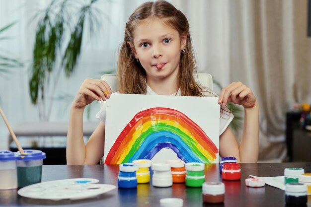 Cute little girl holds painting with colorful rainbow.