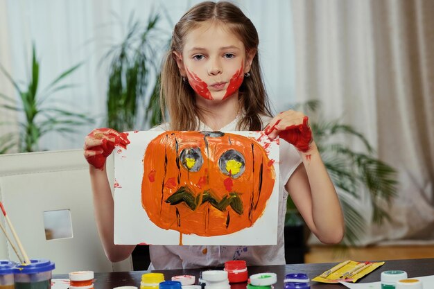 The cute little girl holds a poster with painted Halloween pumpkin.