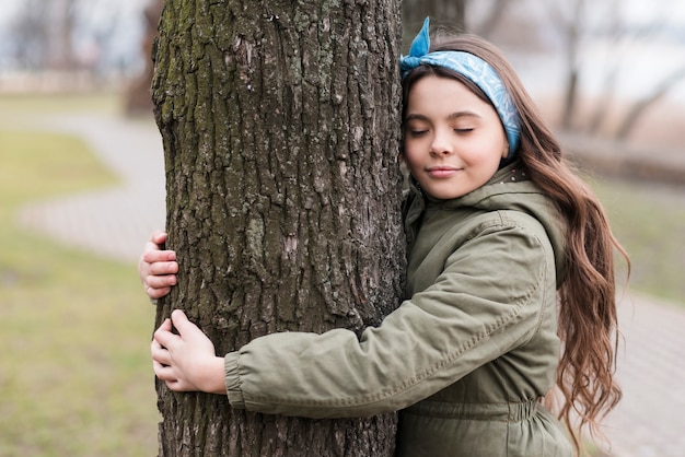 Милая маленькая девочка обнимает дерево