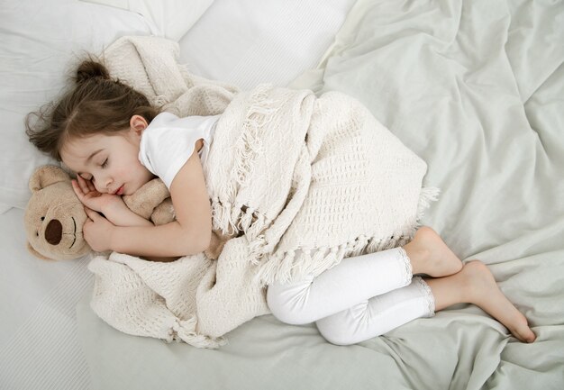 かわいい女の子がテディベアのおもちゃでベッドで寝ています。子供の発達と睡眠の概念。上からの眺め。