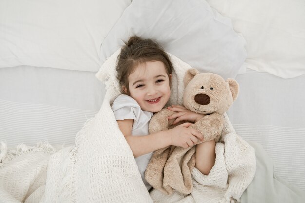 A cute little girl is sleeping in a bed with a Teddy bear toy .