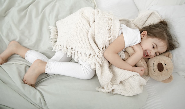 귀여운 소녀가 테디 베어 장난감을 가지고 침대에서 자고 있습니다.