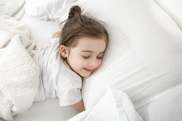 A cute little girl is sleeping in a white bed .