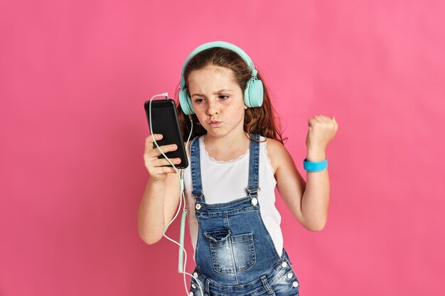 Bambina sveglia che ascolta la musica con un telefono e le cuffie