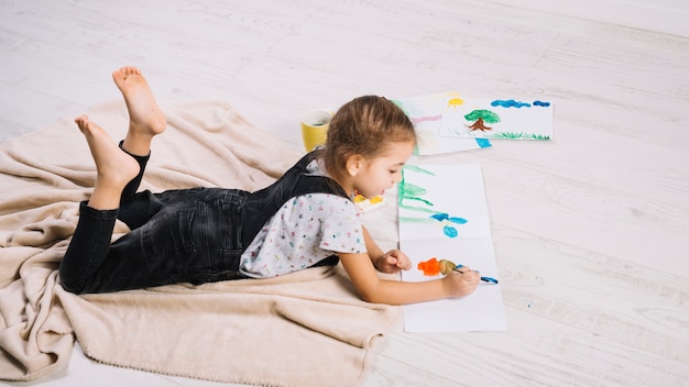 Cute little girl painting with bright aquarelle on floor