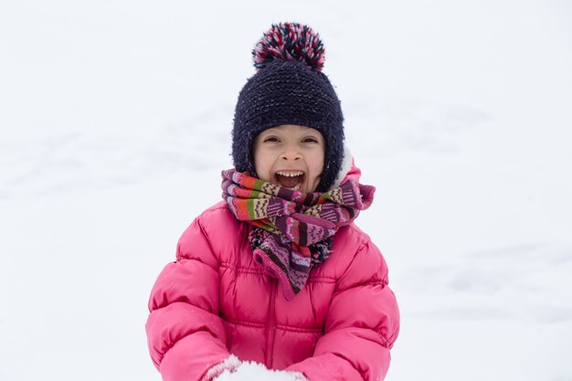 분홍색 재킷과 모자를 입은 귀여운 소녀가 눈 속에서 놀고 있습니다. 겨울 어린이 엔터테인먼트 개념.