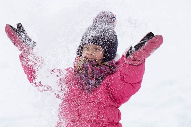 ピンクのジャケットと帽子をかぶったかわいい女の子が雪の中で遊んでいます。冬の子供向けエンターテインメントのコンセプト。