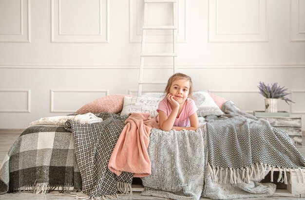 Cute little girl playing on the bed. Looks thoughtfully and rests .