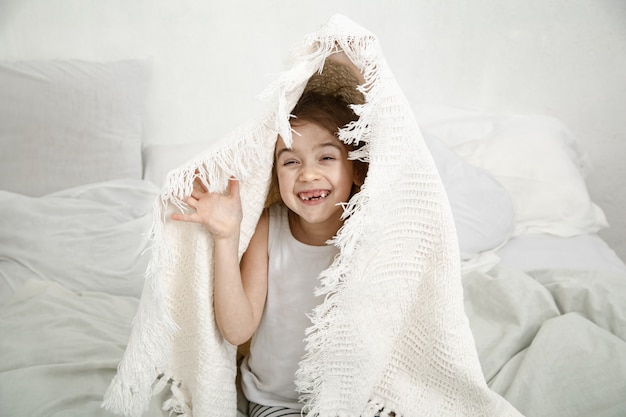 Free photo cute little girl playing in bed with a blanket after sleeping