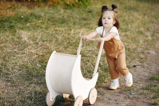 Free photo cute little girl playing in a park with white carriage