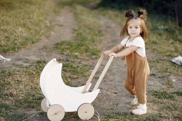 Милая маленькая девочка, играя в парке с белой коляской