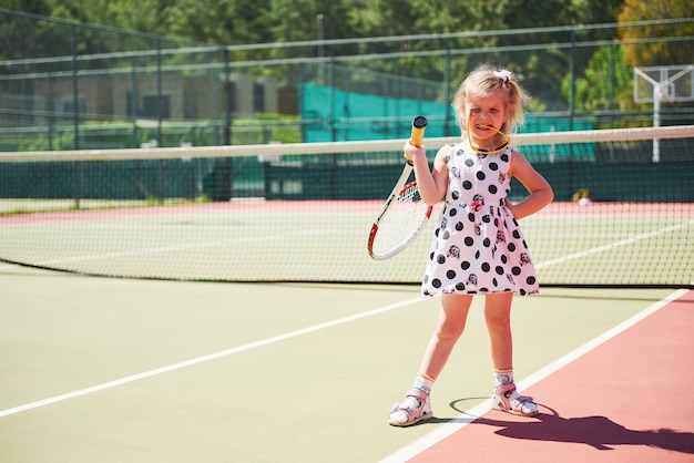 Free photo cute little girl playing tennis on the tennis court outside.