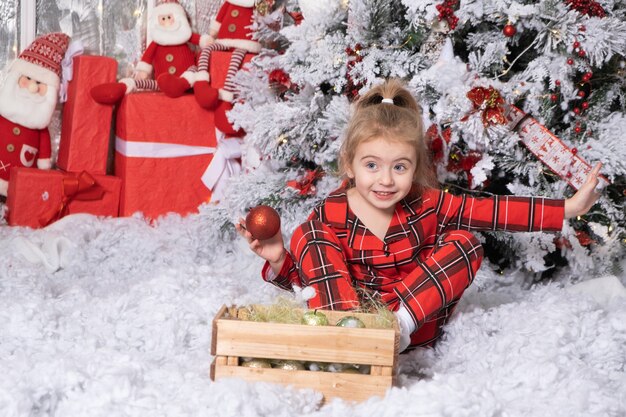 Cute little girl playing with christmas balls in christmas decorated room. merry christmas concept.